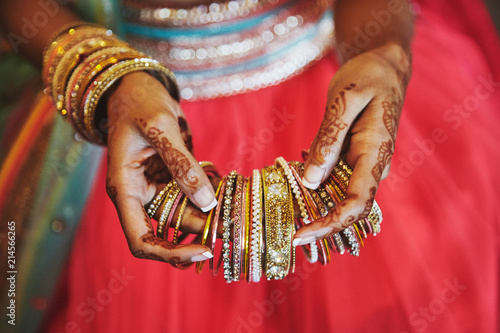 The hand with mehndi of Indian bride holding a lot of glitter bracelets (bangle) with red legenha background, close-up
