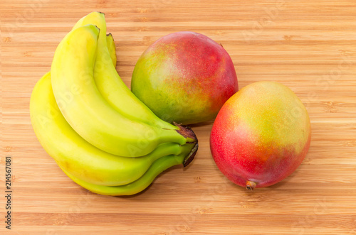 Two whole mango fruit and bananas on a wooden surface