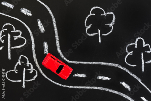 Fototapeta Naklejka Na Ścianę i Meble -  Red toy car on a blackboard with chalk drawn road and trees.