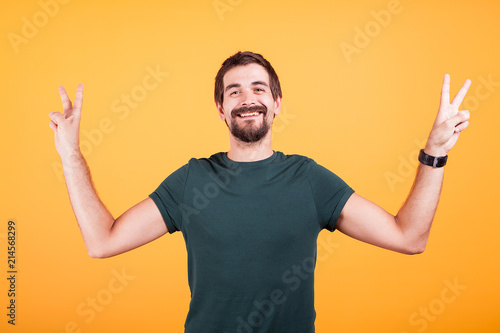 Happy smiling man showing victory peace sign with both hands isoalted on yellow background in studio