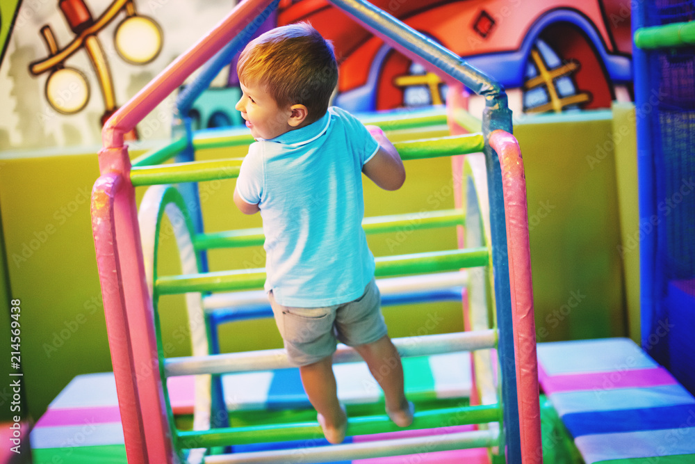 Fototapeta premium Cute little boy in a blue T-shirt is playing on a children's playground indoors.