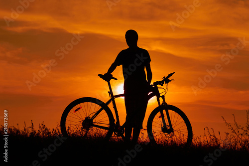 Silhouette of a young man with a bicycle at sunset.