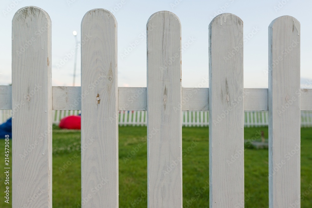 Decorative wooden fence painted white. A green lawn behind fence.