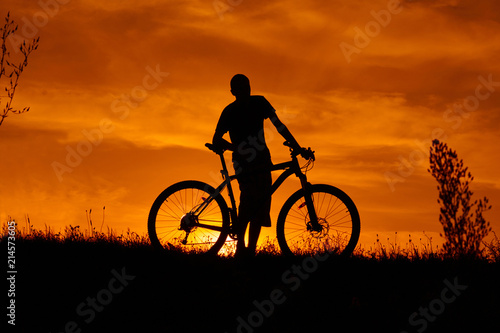 Silhouette of a young man with a bicycle at sunset.