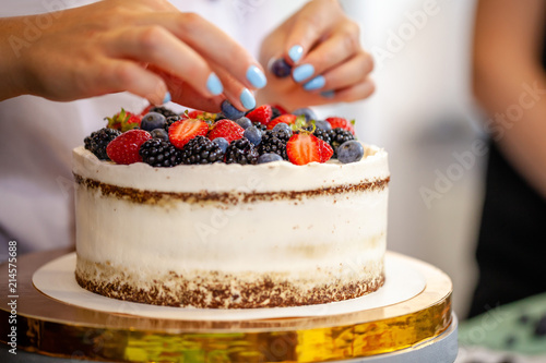 Photography Girl chef cooks confectioner, decorates cake with forest berries