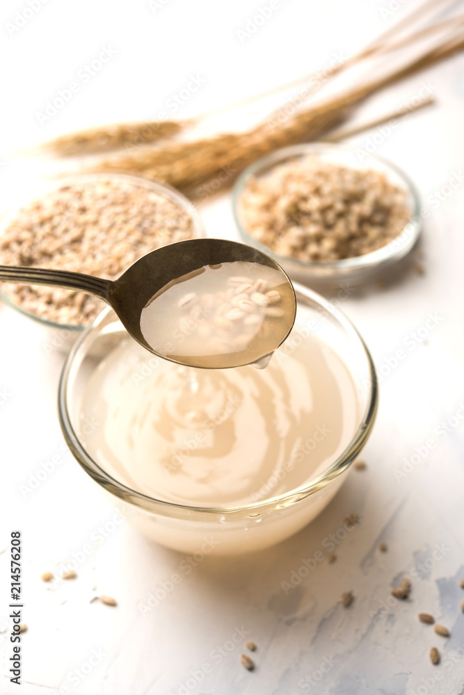 Barley water in glass bowl with spoon and raw and cooked pearl barley wheat/seeds. selective focus Barley water in glass bowl with spoon and raw and cooked pearl barley wheat/seeds. selective focus