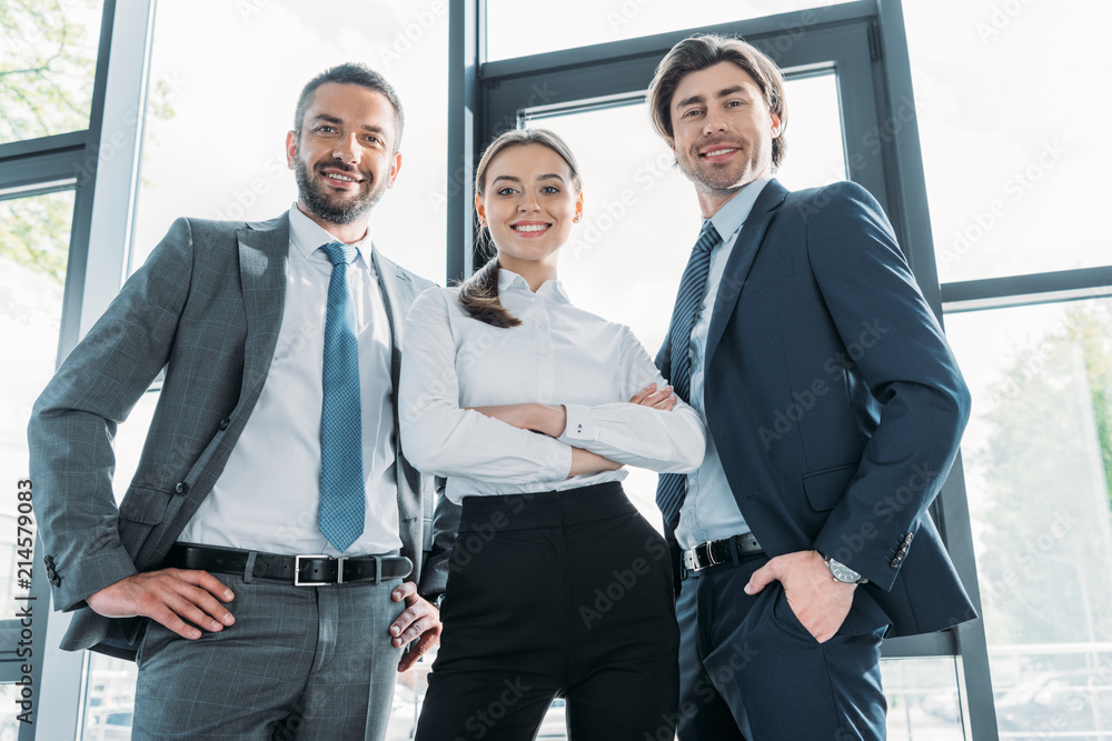 bottom view of group of smiling young business people standing at modern office and looking at camera bottom view of group of smiling young business people standing at modern office and looking at camera