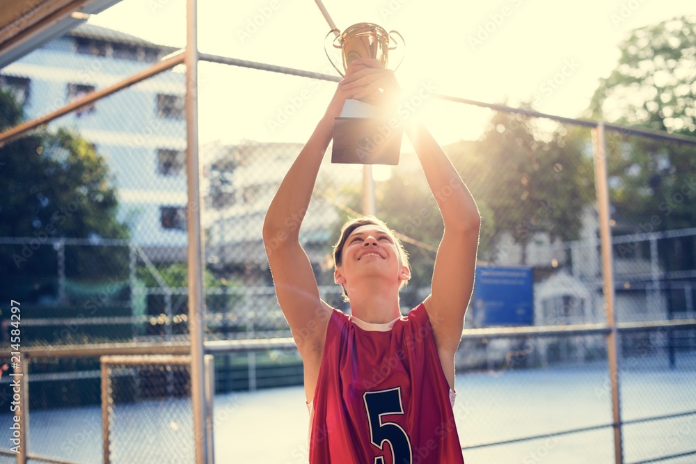 Caucasian teenage boy in sporty clothes holding up a trophy outdoors