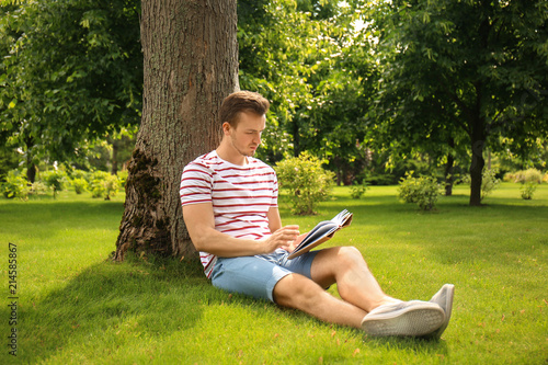 Young man reading book while sitting near tree in park © Pixel-Shot