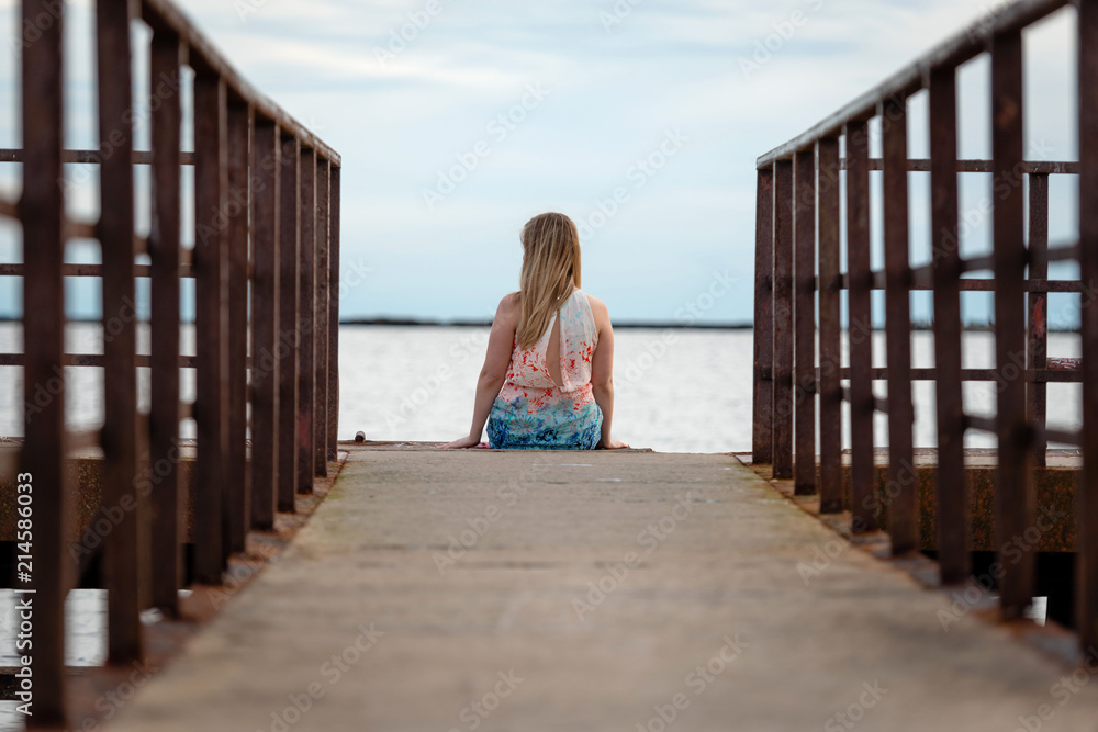 Woman is sitting on the platform and looking at the sea. View from the back. Woman is sitting on the platform and looking at the sea. View from the back.