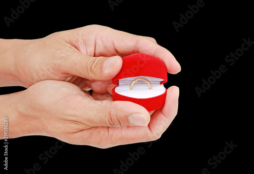 Hand holding red gift box with gold wedding ring isolated on black background.