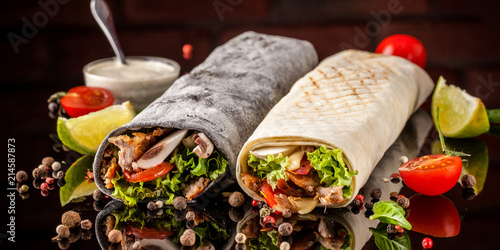 Two burrito, black and white lavash with chicken, mushrooms, salad, cherry tomatoes, lime, and salsa. Copy space, selective focus