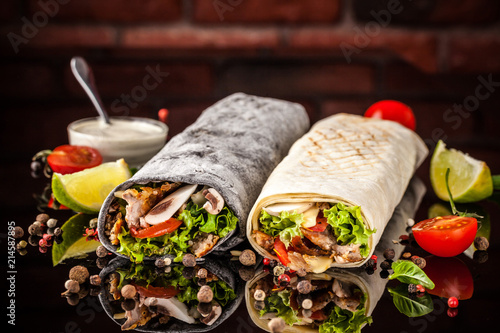 Two burrito, black and white lavash with chicken, mushrooms, salad, cherry tomatoes, lime, and salsa. Copy space, selective focus photo