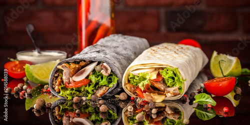 Two burrito, black and white lavash with chicken, mushrooms, salad, cherry tomatoes, lime, and salsa. Copy space, selective focus photo