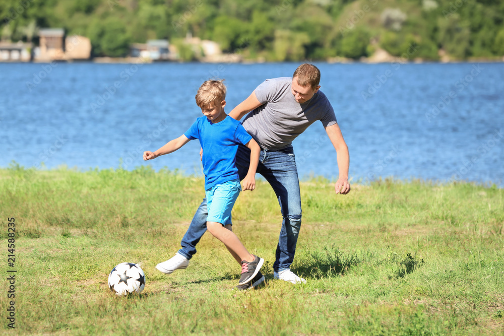 Obraz premium Happy father and son playing football near river