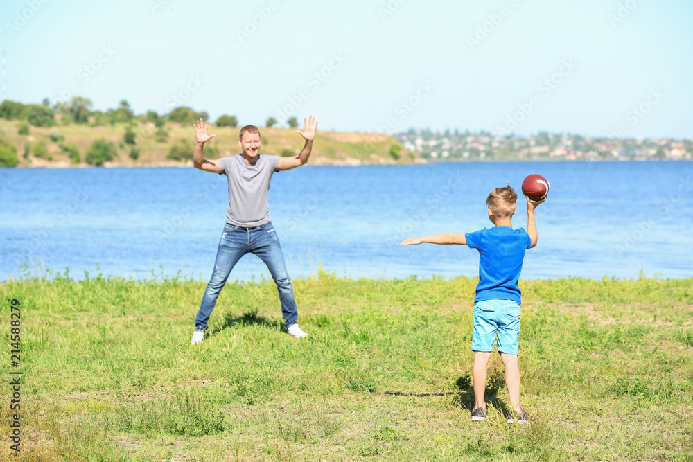 Obraz premium Happy father and son playing rugby near river
