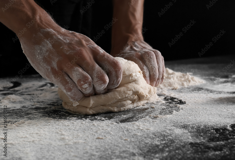 Man kneading dough on black background
