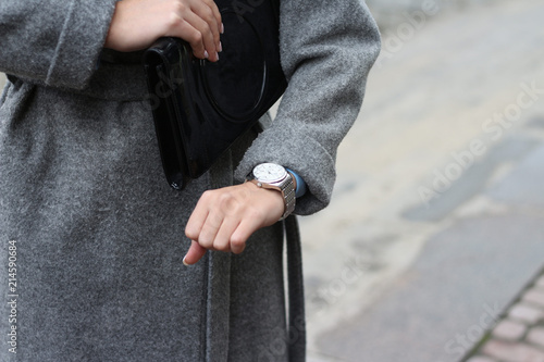 a young girl in a gray coat looks at her wristwatch  checks the time  looks at her watch. hurry to a meeting  be late. punctuality.keep to the plan