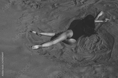 Sexy woman or girl in seductive sexy body suit lying on the sand in the desert or on the beach. Concept of leisure, travel and vacation. monochrome black and white picture