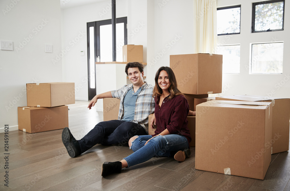 Portrait Of Happy Couple Sitting On Floor Surrounded By Boxes In New Home On Moving Day Portrait Of Happy Couple Sitting On Floor Surrounded By Boxes In New Home On Moving Day