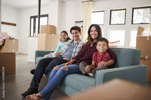 Portrait Of Happy Family Resting On Sofa Surrounded By Boxes In New Home On Moving Day