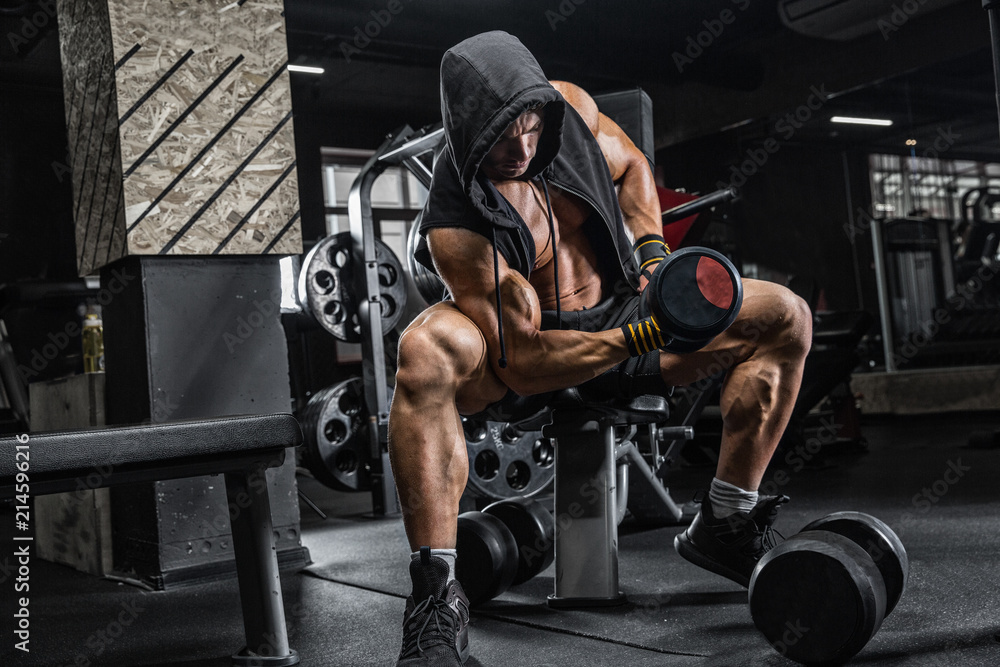 The brutal man is training the biceps on the bench, using a dumbbell.  Concept - personal trainer, diet, sports nutrition, crossfit, styrodes,  dumbbells, bodybuilding, weightlifting, gym. Stock Photo | Adobe Stock