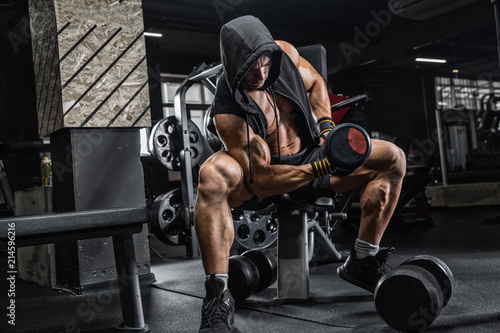 The brutal man is training the biceps on the bench, using a dumbbell. Concept - personal trainer, diet, sports nutrition, crossfit, styrodes, dumbbells, bodybuilding, weightlifting, gym.