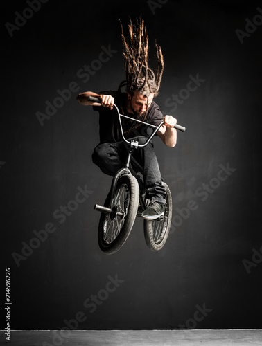 Young man with dreadlocks jumping on his BMX bike.
