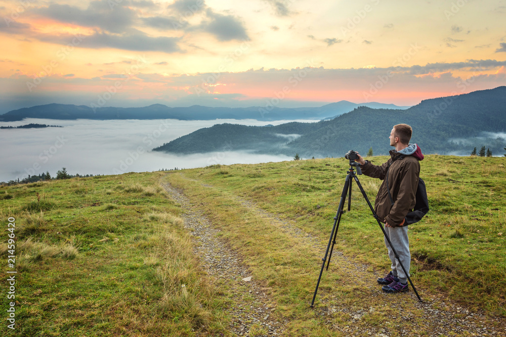 Professional photographer takes photos with camera on tripod on rocky peak.