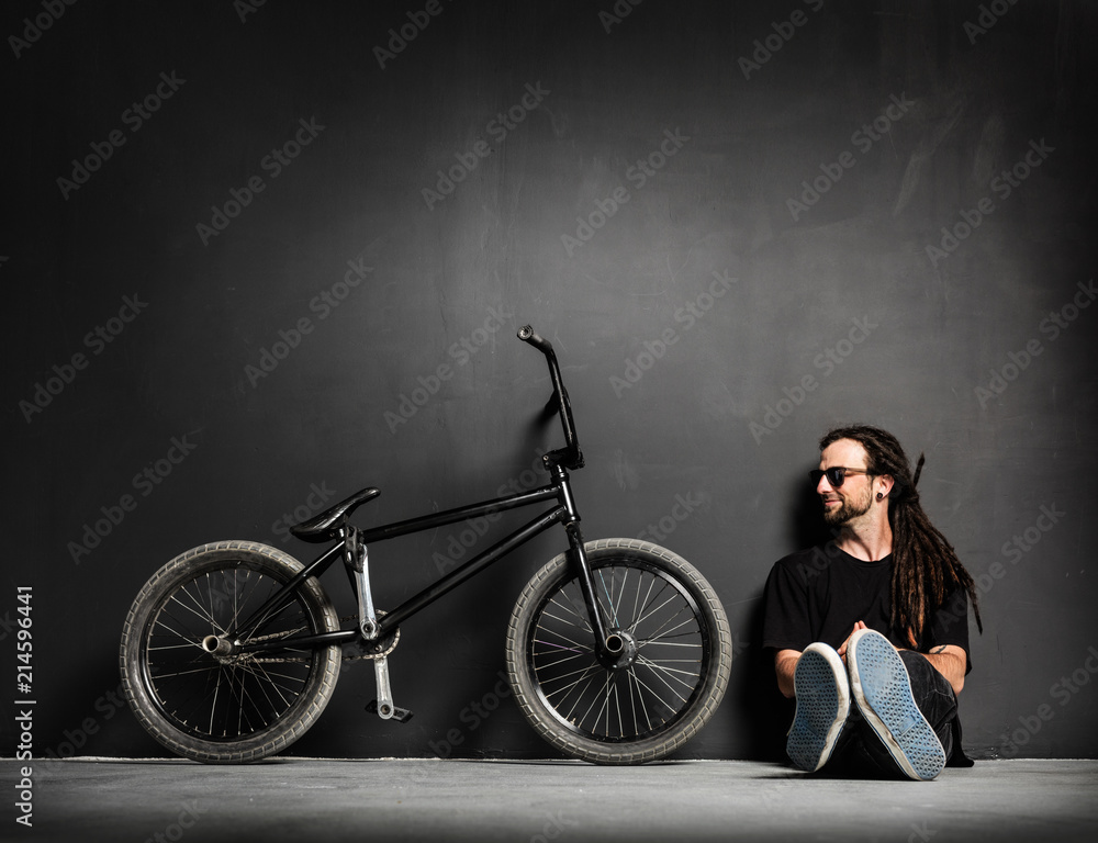 Obraz premium Young smiling man sitting next to his BMX bike.