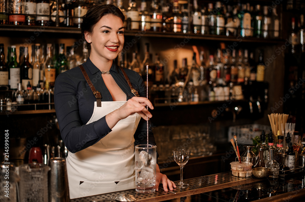 Smiling female bartender mixing an ice in the glass