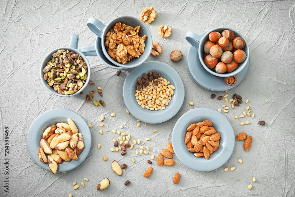 Cups and plates with different nuts on textured background