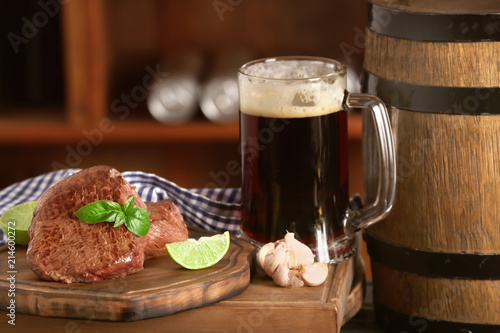 Mug of delicious beer and grilled steaks on wooden board