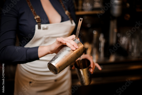 Bartender girl pourring a cocktail drink from one steel cup to another