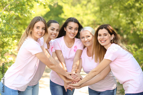 Beautiful women of different ages with pink ribbons putting hands together outdoors. Breast cancer concept