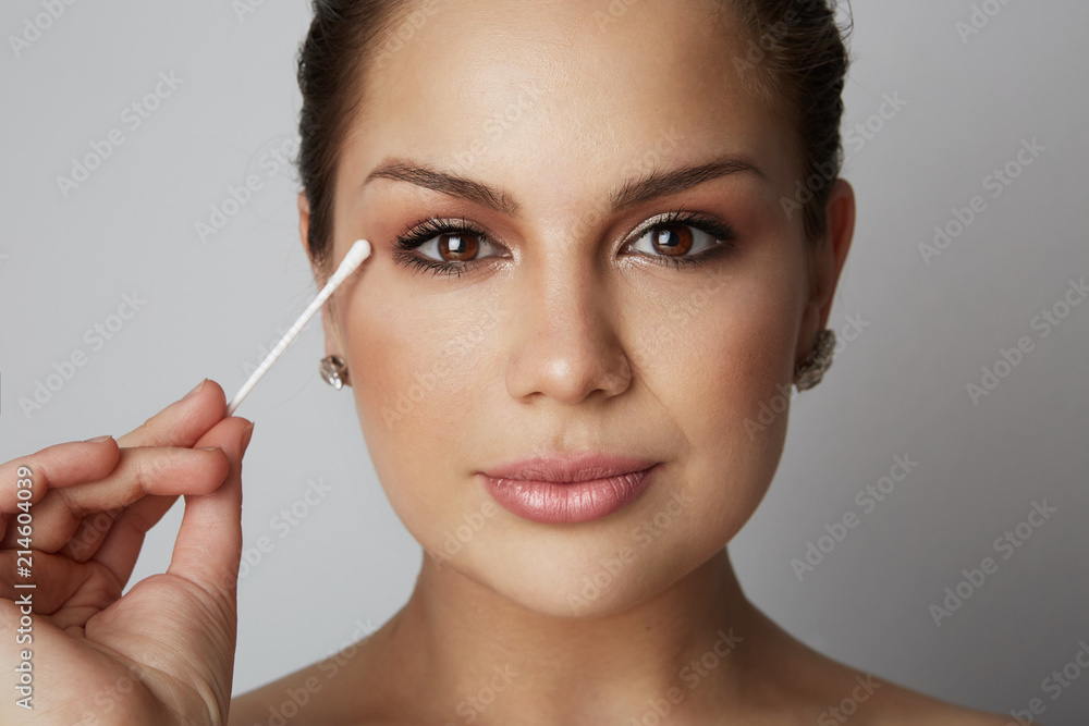 Portrait Handsome beauty girl refreshing skin face with white cotton buds over gray studio background.Model with light nude make-up.Healthcare skin makeup concept Portrait Handsome beauty girl refreshing skin face with white cotton buds over gray studio background.Model with light nude make-up.Healthcare skin makeup concept
