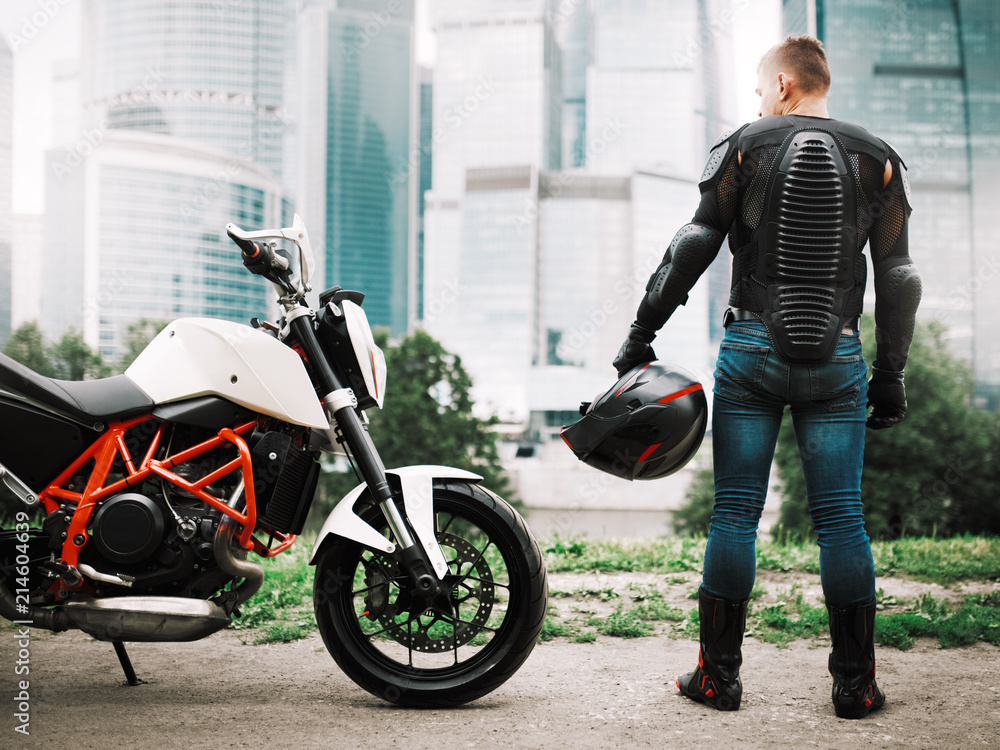 Fototapeta premium Rowerzysta z kaskiem w rękach i motocyklem w pobliżu dzielnicy miejskiej w centrum miasta
