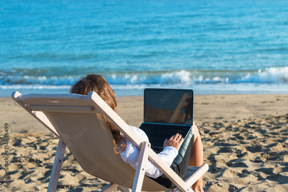 Young woman in office clothes with a laptop on the beach on a background of the sea in a summer sunny day. Concept