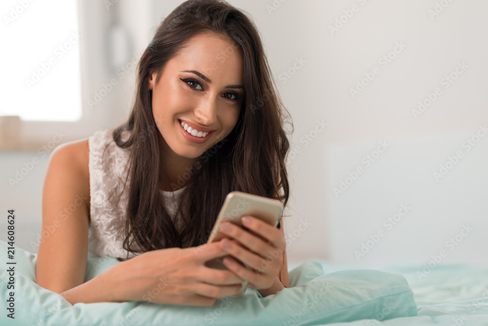 Smiling woman using cell phone in bed Smiling woman using cell phone in bed