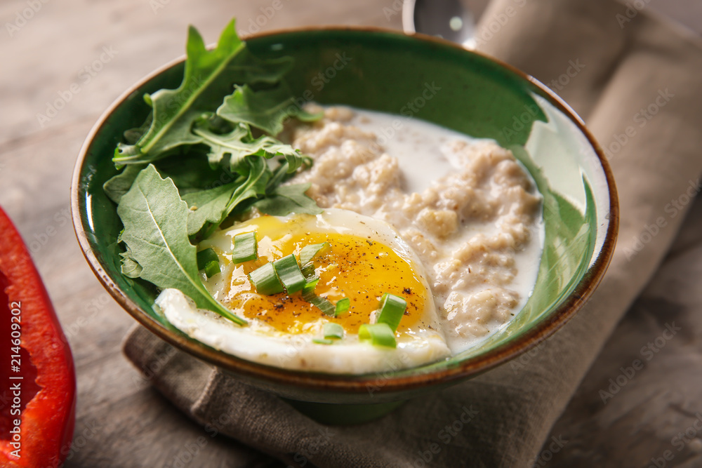 Bowl with tasty oatmeal and fried egg on wooden table