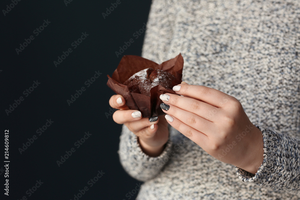 Fototapeta premium Young woman with beautiful manicure holding muffin on dark background, closeup