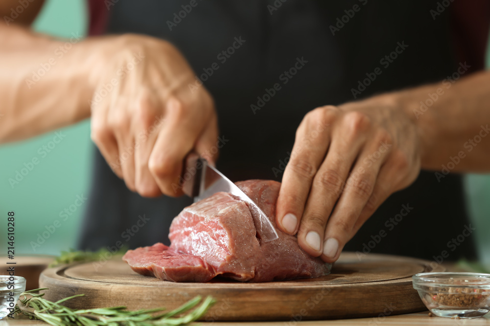 Man cutting raw meat on board in kitchen, closeup