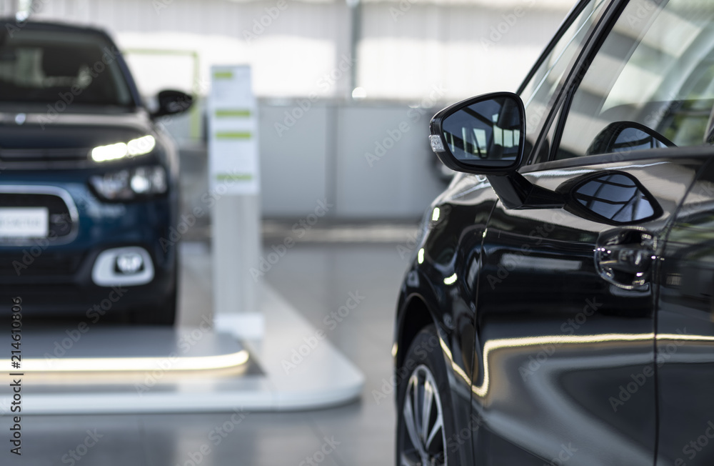 Close-up photo of shiny car and another one in blurred background standing in bright car rental interior