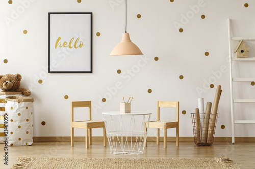 Bright and natural interior of a kindergarten room with a small table and wooden chairs against the wall with dot stickers and poster. Real photo