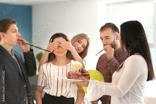 Happy colleagues presenting cake to young woman on her birthday in office