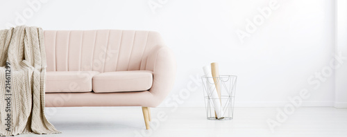 Real photo of white living room interior with metal basket with paper rolls and pastel pink couch with coverlet © Photographee.eu