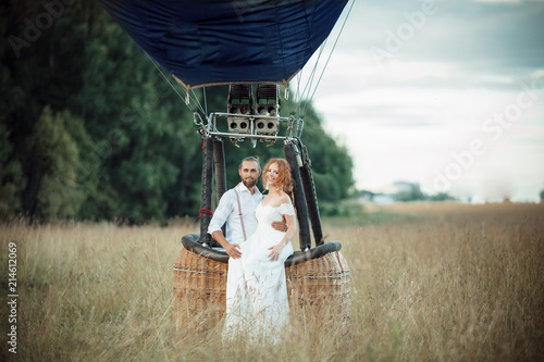 Happy wedding couple are sitting inside airballoon basket in the sunny field. photo