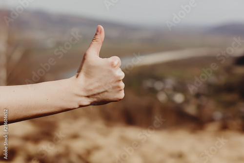 woman hand showing like with thumb up on background of sunny mountains, approval and travel concept © sonyachny