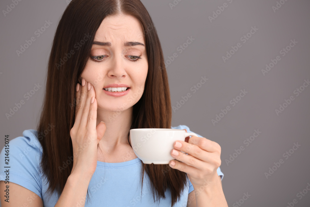 Young woman with sensitive teeth and cup of hot coffee on grey background Young woman with sensitive teeth and cup of hot coffee on grey background