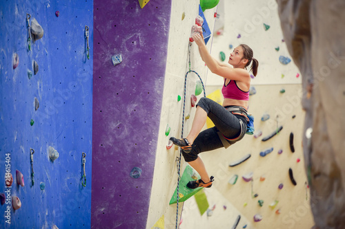 Photo of athlete girl climbing up purple wall for rock climbing